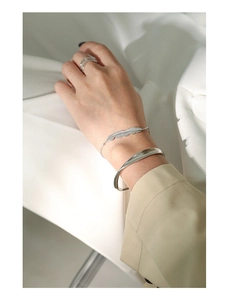 Detail view of minimalist silver bangle, feather bracelet and layered ring set on wrist