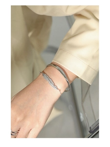 Close-up of minimalist silver feather charm bracelet and sleek open bangle on wrist