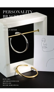 Detail of silver snake-pattern cuff and gold twisted bracelet on marble display stand