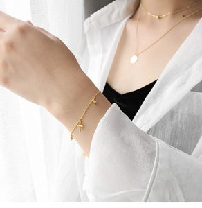 Dettaglio del bracciale con croce dorata e collane a strati su polso e collo della modella