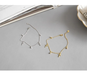 Dettaglio di bracciali a croce in oro e argento con zirconi su sfondo minimalista