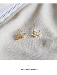 Κοντινό πλάνο χρυσά σκουλαρίκια γερανός origami σε λευκό λινό ύφασμα