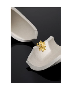 Close-up of golden clover-textured S925 silver ear clip on a high-contrast dark background