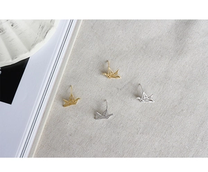 Λεπτομερής προβολή σκουλαρικιών γερανός origami σε χρυσό και ασήμι σε λινό ύφασμα