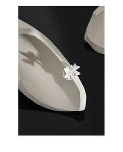 Detailed view of silver four-leaf clover ear clip on grey stone with reflections