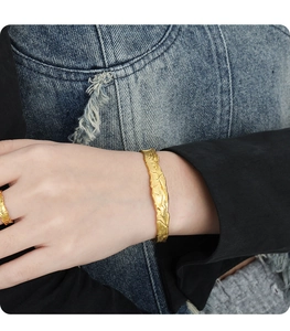 Dettaglio del bracciale rigido dorato regolabile con texture lava su sfondo denim