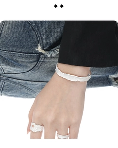 Dettaglio del bracciale e degli anelli in argento con texture irregolare su denim