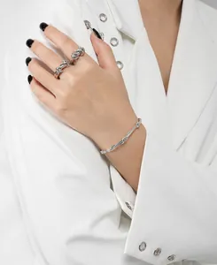 Detail view of silver twisting vine bracelet and rings styled with a white blazer