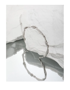Close-up of silver vine-style intertwined knot cuff bracelet on a minimalist stone base