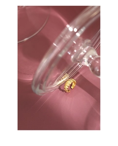 Goldener Croissant-Ring hinter Glas auf altrosa Hintergrund in eleganter Präsentation