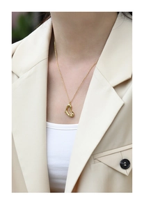 Nahaufnahme einer goldenen Herzkette mit unregelmäßigem Design an einem Model in Beige