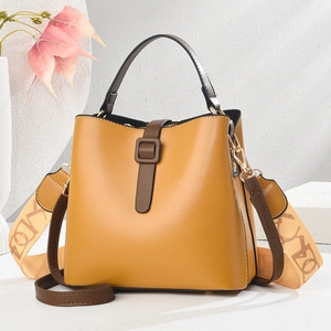 Elegante borsa a secchiello giallo senape con doppia tracolla e manico marrone su sfondo bianco