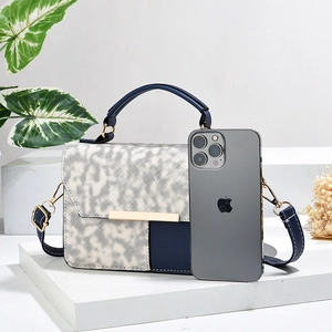 Sac bandoulière bicolore en cuir et texture tissée avec fermoir doré sur socle blanc