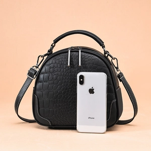 Black crocodile pattern handbag with handle and adjustable strap next to a phone for size