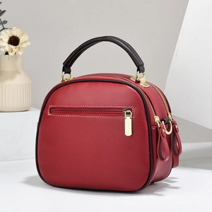 Detail of red pebbled leather crossbody bag featuring dual main zipper pockets and gold hardware