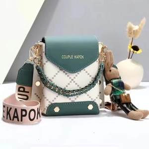Detail of crossbody bag with green leather flap, patterned strap, and bunny charm