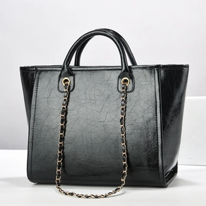 Detail of black oil-wax textured tote bag with golden chain strap and round handles