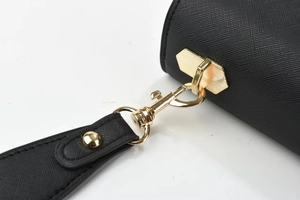 Détail macro du fermoir doré et du cuir à grain croisé sur le sac à main noir