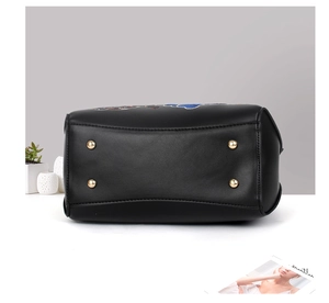 Détail de la base du sac à main en cuir noir avec quatre pieds dorés et broderie élégante