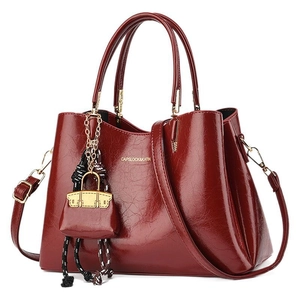 Polished burgundy leather tote bag with gold logo and mini charm on white background
