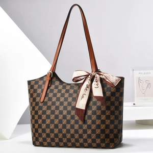 Close-up of a checkered tote bag with brown leather handles and decorative scarf detail