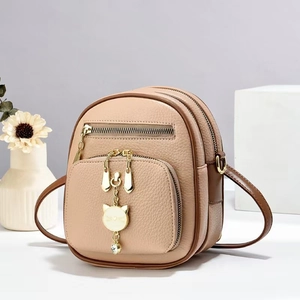 Detail of light brown faux leather mini backpack with gold cat charm and dual zip texture