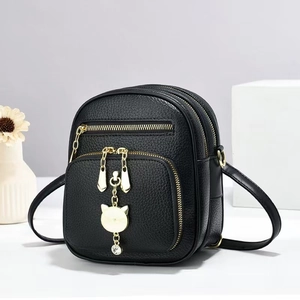 Detail of black faux leather mini bag with gold cat pendant and multi-zip texture