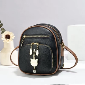 Detail of black pebbled leather mini bag with gold cat charm and contrast brown trim