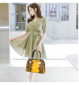 Detail view of bright yellow snakeskin textured handbag with black top handle and silver hardware