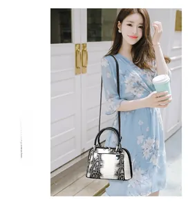 Detail of structured faux snakeskin handbag with dual top handles and long shoulder strap