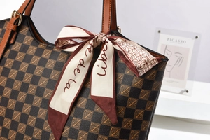 Detail of checkered tote bag featuring a leather handle, silk scarf, and gold metal hardware