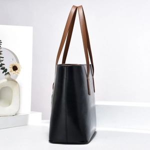 Vue latérale du grand sac cabas en cuir noir avec anses marron sur socle géométrique blanc