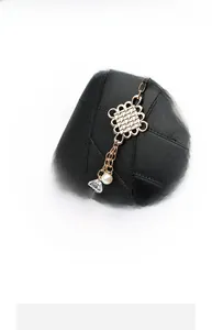Detail of black leather handbag featuring golden knot charm with pearl and crystal tassel