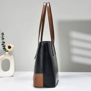 Side view detail of a high-capacity black leather tote bag with brown contrast trim