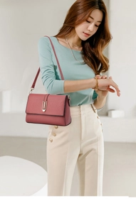 Detail of dusty pink pebbled leather crossbody bag with elegant gold metal bar accent