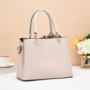 Close-up of beige handbag with vertical pleats, gold hardware and decorative silk scarf