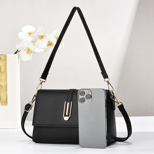 Close-up of black pebble leather crossbody bag next to a phone for size comparison