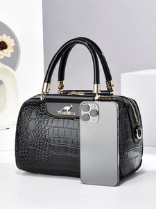 Detail of black crocodile embossed handbag with gold hardware and smartphone for scale
