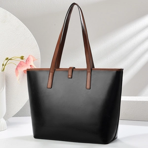 Detail of the minimalist black tote bag featuring contrasting brown leather handles and buckle