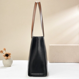 Side view of structured black tote bag with brown leather handles and minimalist decor