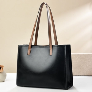 Detail of a large black PU leather tote bag with brown textured handles and clean stitching