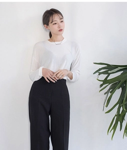 Top bianco a maniche lunghe e pantaloni neri a gamba larga su modella con foglie verdi