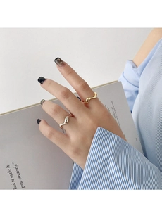 Détail de bagues ondulées minimalistes en argent et or portées avec un livre