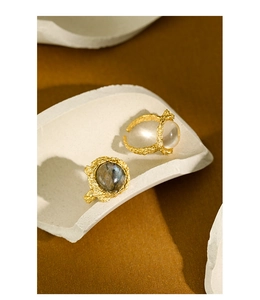 Close-up of gold lava texture rings with labradorite and opal stones on a ceramic prop