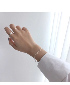 Close-up of minimalist S925 sterling silver layered rings and a beaded chain bracelet