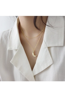 Dettaglio di collana dorata a strati con luna a texture irregolare su camicia bianca