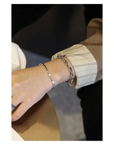 Close-up of minimalist silver chain bracelets set styled with a retro ring on wrist