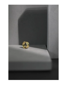 Detailopname van een brede minimalistische vergulde ear cuff op een grijze steen