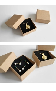 Detail van gouden ketting en pareloorbellen in een bruine kraft papieren doos