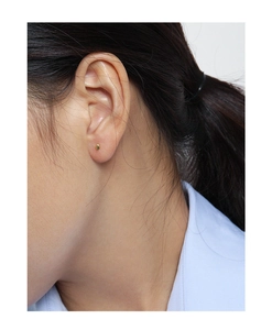 Détail d'une puce d'oreille boule dorée minimaliste portée avec un éclat métallique poli